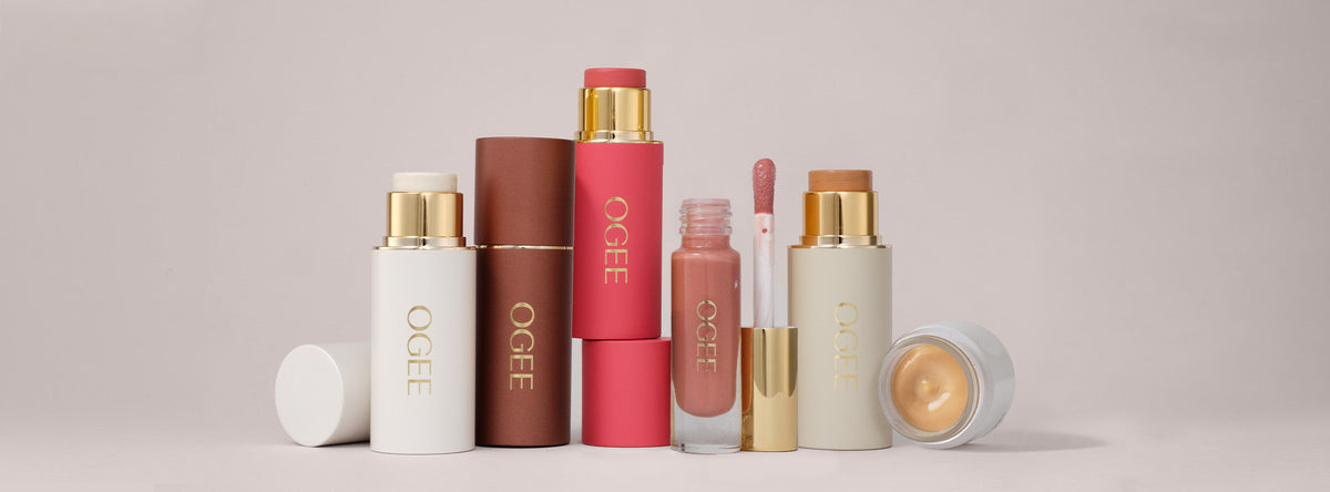 Several Ogee makeup sticks, lip gloss, and a cream jar arranged on a light background.
