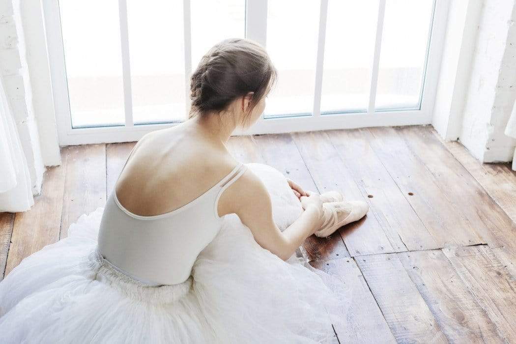 Graceful ballerina in a bright studio tying ballet slippers