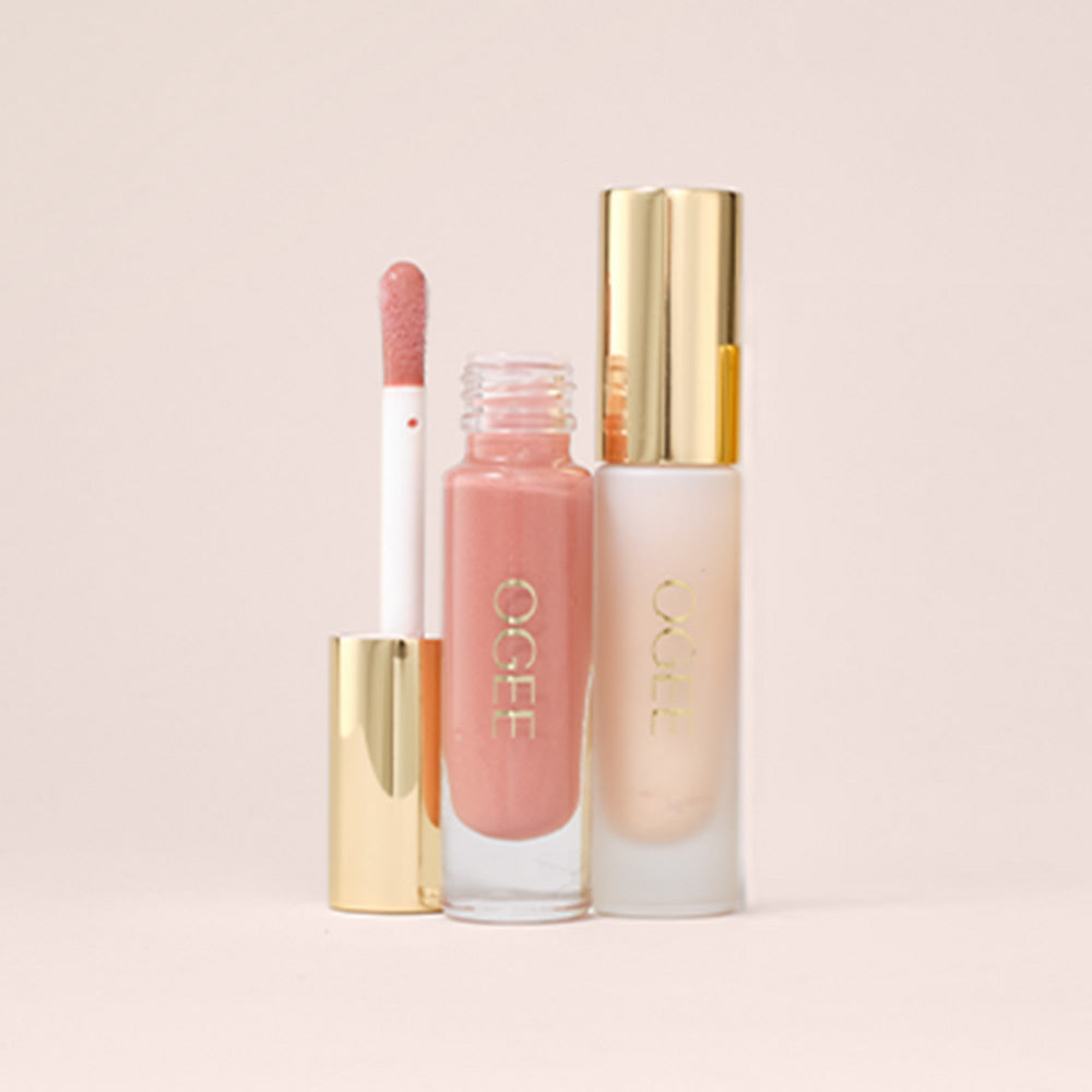 An open tube of pink Ogee lip gloss with its doe-foot applicator and gold cap beside it, next to a frosted Ogee lip gloss bottle with a gold cap, on a blush pink background.